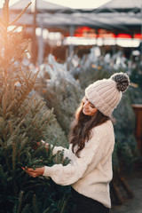 Obraz premium Elegant girl buys a Christmas tree. Woman in a white knited sweater. Beautiful lady with dark hair.