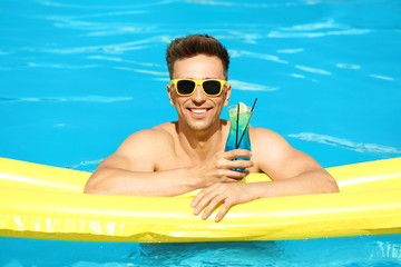 Happy young man with cocktail and inflatable mattress in swimming pool