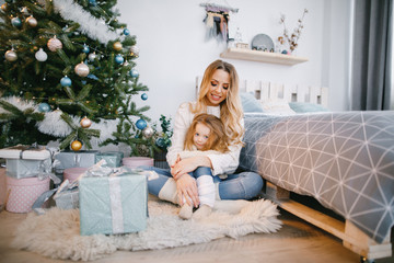 mother hugging daughter and sitting by the christmas tree