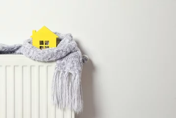 Fotobehang House model wrapped in scarf on radiator indoors, space for text. Winter heating efficiency © New Africa