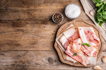 Board with slices of raw bacon on wooden table, flat lay. Space for text