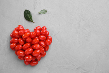 Heart made of fresh goji berries and leaves on grey background, flat lay. Space for text