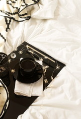 Christmas or New Year flat lay top view coffee cup and Xmas holiday decorations on black tray in bed with lights. Copy space