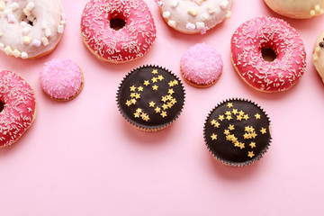 Various types of donuts and other cakes on pink background.