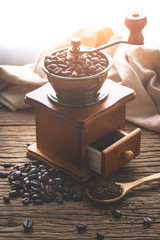 coffe bean with grinder and coffee in wooden spoon on wood table in morning light.