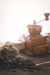 coffe bean with grinder and coffee in wooden spoon on wood table in morning light.