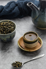 A cup of hot green tea with dry leaves in spoon on cement table. Healthy drink concept.