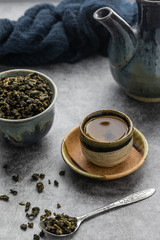 A cup of hot green tea with dry leaves in spoon on cement table. Healthy drink concept.