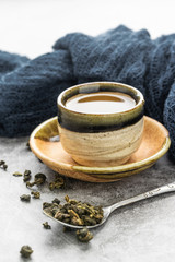 A cup of hot green tea with dry leaves in spoon on cement table. Healthy drink concept.