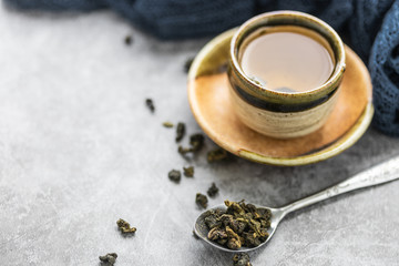 A cup of hot green tea with dry leaves in spoon on cement table. Healthy drink concept.