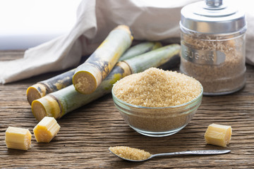 Brown sugar in bowl with spoon and sugar cane on wooden table.
