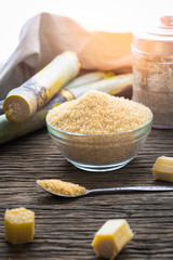 Brown sugar in bowl with spoon and sugar cane on wooden table.