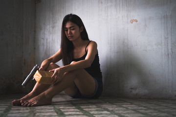 Low key portrait of young Asian woman is holding gun and drugs in the old room. Social problems, crime and drugs concept.