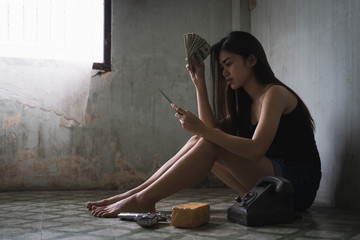 Low key portrait of young Asian woman is holding knife and banknotes in the old room. Social problems, crime and drugs concept.