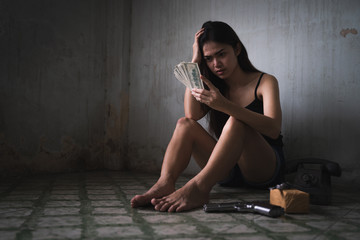 Low key portrait of young Asian woman is worrying a lot and holding banknote in the old room. Social problems, crime and drugs concept.
