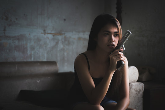 Low key portrait of beautiful Asian woman is holding gun in the old room. Social problems, crime and drugs concept.