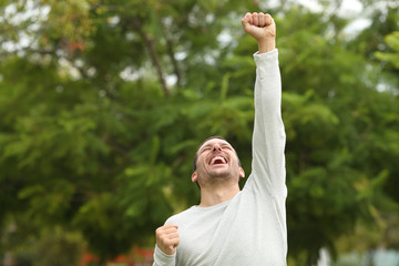 Excited man raising arm celebrating success in a park