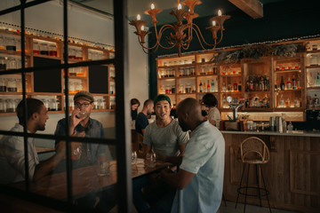 Diverse group of guys talking over drinks in a bar - obrazy, fototapety, plakaty