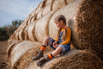 Cute girl having fun on rolls of hay bales in field
