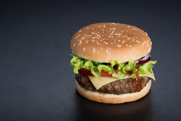 Hamburger with a double serving of meat, tomatoes, salad, onions on a wooden board in a restaurant.Copy space