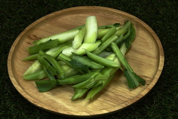 Fresh organic Chinese kale on the wood plate. Chopped (sliced) Chinese kale on the grass background.