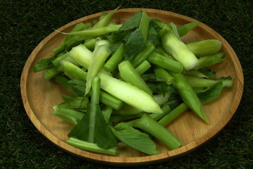 Fresh organic Chinese kale on the wood plate. Chopped (sliced) Chinese kale on the grass background.