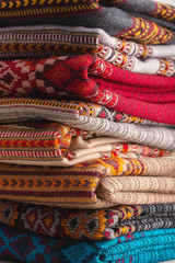 On the table lies pyramid of colorful rugs in warm colors. Clothes for cold weather. Close-up.