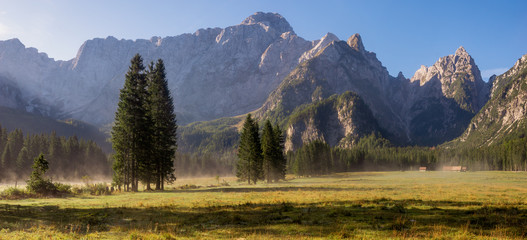 meadow under the Alpine peaks during a sunny, foggy morning