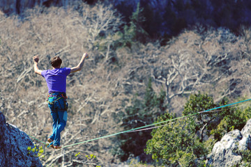 Obraz premium A man is walking along a stretched sling. Highline in the mountains. Man catches balance. Performance of a tightrope walker in nature. Highliner on the background of the mountains.