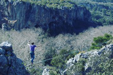 A man is walking along a stretched sling. Highline in the mountains. Man catches balance. Performance of a tightrope walker in nature. Highliner on the background of the mountains.