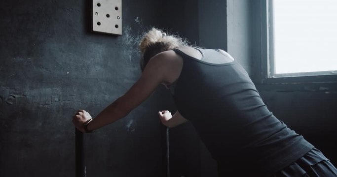 Young athletic blonde woman is exhausted and breathing heavy after extreme power exercising in large gym slow motion.