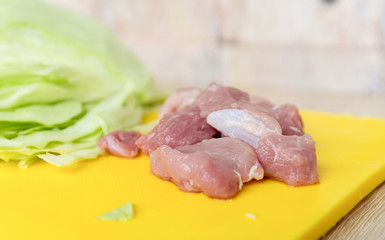 Raw fresh meat on a cutting board, ready to be cooked, cabbage in backgrond. Selectie focus.