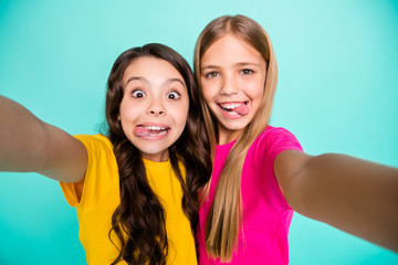 Photo of two glad fooling cute casual girls showing tongues to camera while isolated with teal...