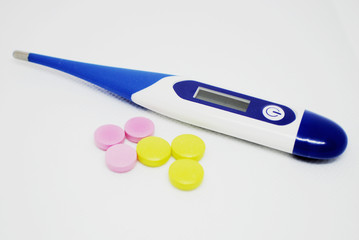  The thermometer and multi-colored pills on a white background