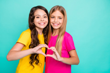 Photo of two embracing girls shaping heart with their hands while isolated with teal background
