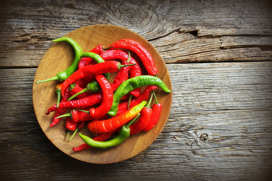 Wooden bowl with red, chilli pepers on rustic dark background.