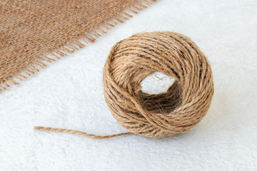 Natural hemp cord ball and burlap on a rough white surface. Roll of jute string or flax twine. Coarse rustic thread for souvenirs, macrame, craft or garden work.