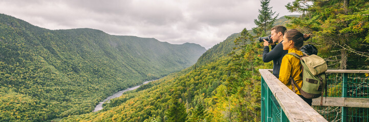 Fototapeta premium Podróżować para turystów pieszych robienia zdjęć z aparatem w widoku górskiego krajobrazu w lesie jesienią Parc de la Jacques Cartier, Quebec, Kanada. Tło transparent panoramy.