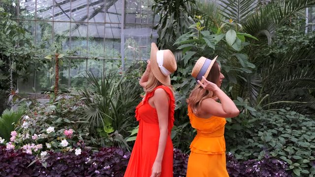 Sisters stand close to each other. Women have a photo shooting in botanic garden. The girls have blonde hair.