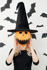 Young woman in conical hat holding orange balloon woth creepy smiling face in front of her head