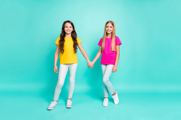 Fototapeta premium Full length body size photo of two nice cute beautiful kind friendly girls holding each other hands while isolated with teal background