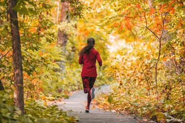 Gordijnen Run vrouw joggen in buiten herfst herfst gebladerte natuur achtergrond in bos. Trail running runner atleet training cardio buitenshuis, oranje kleuren boombladeren. © Maridav