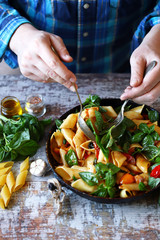 Selective focus. Chef's hands mix pasta with basil and tomatoes.
