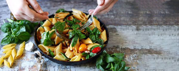 Selective focus. Chef's hands mix pasta with basil and tomatoes.