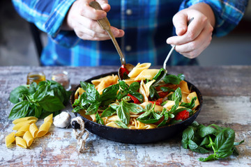 Selective focus. Chef's hands mix pasta with basil and tomatoes.