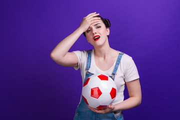 Puzzled young girl football fan watching match support favorite team with soccer ball, isolated on blue background.