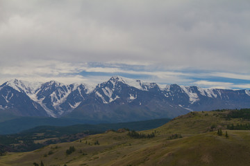 Snow top in Altai mountains. Bottom view. Summer travel concept. Dark day with clouds.