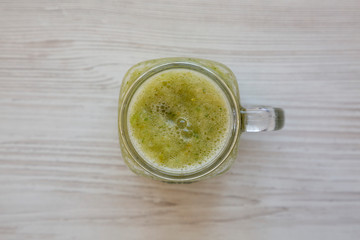 Homemade green cucumber apple smoothie in a glass jar on a white wooden background, top view. Flat lay, overhead, from above. Close-up.