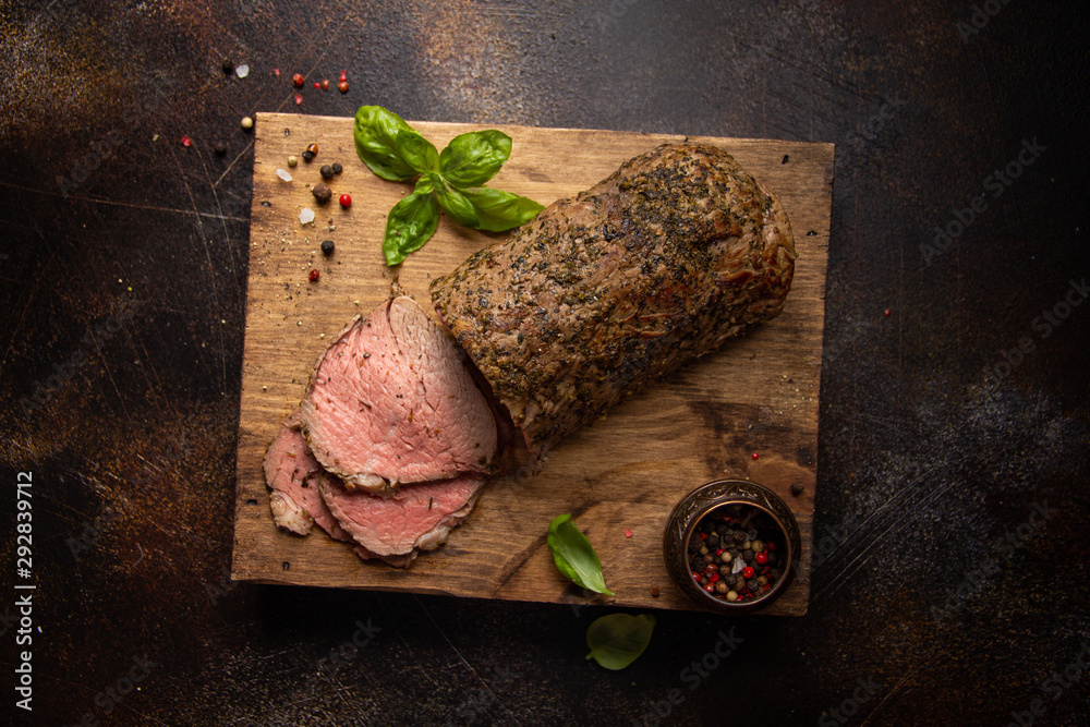 Wall mural juicy roast beef with spices sliced on a cutting board, delicious meat, traditional food. on dark ba