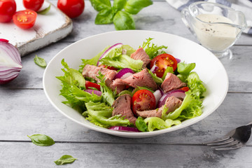 Salad with roast beef, tomato, onion, lettuce and mustard sauce on light background. Delicious healthy lunch with meat, diet food